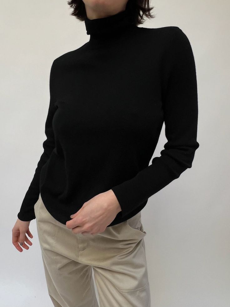 Lovely finely knit turtleneck sweater in an onyx tone. The sweater is a staple in the wintertime, perfect for layering under a favorite blazer, or styled under a crewneck sweater. Material not listed, assuming cotton blend Recommended for size xs-m, depending on the desired fit. Modeled on small frame. Please refer to the measurements listed below: Measures approximately: 16" shoulder to shoulder / 36" bust / 24" sleeve length / 23" shoulder to hemline One inch spot of distressing at the shoulde High Neck Cashmere Sweater For Winter, Winter High Neck Cashmere Sweater, Chic Winter Turtleneck With Ribbed Cuffs, Trendy Black Knit Turtleneck, Winter Cashmere Top, Cashmere Tops For Winter, Versatile Stretch Sweater For Layering, High Neck Cashmere Sweater For Fall, Workwear Ribbed Cashmere Turtleneck