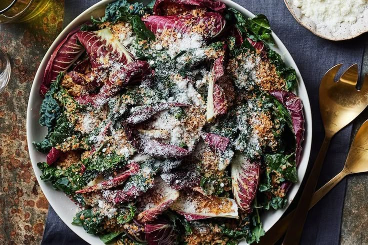 a salad with meat, cheese and greens in a white bowl on top of a table