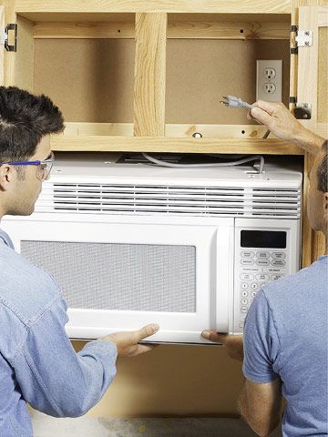 two men are working on an appliance that is built into the wall above them