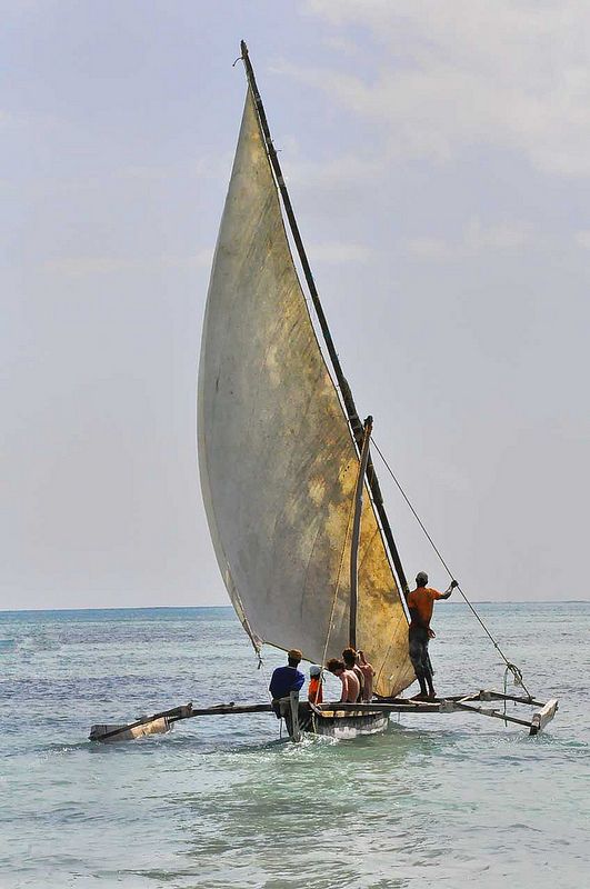 three people on a small sailboat in the ocean with one person standing on it