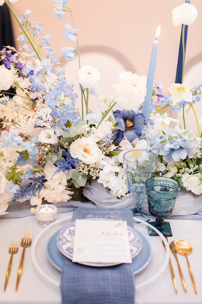 the table is set with blue and white flowers, silverware, and napkins