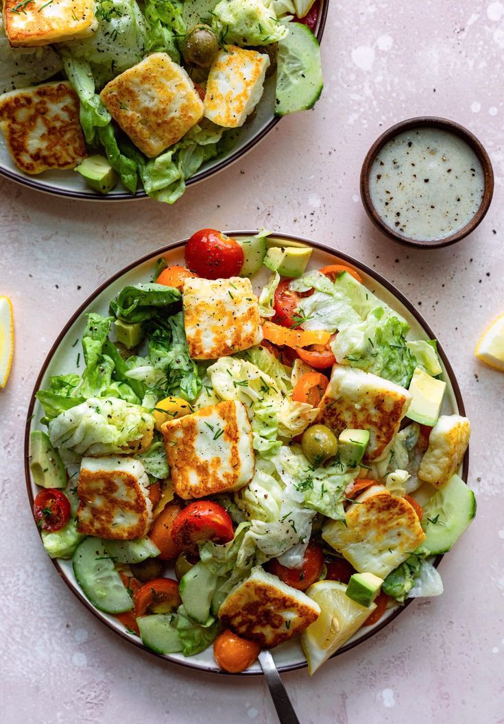 two plates filled with salad next to lemon wedges and seasoning on the side