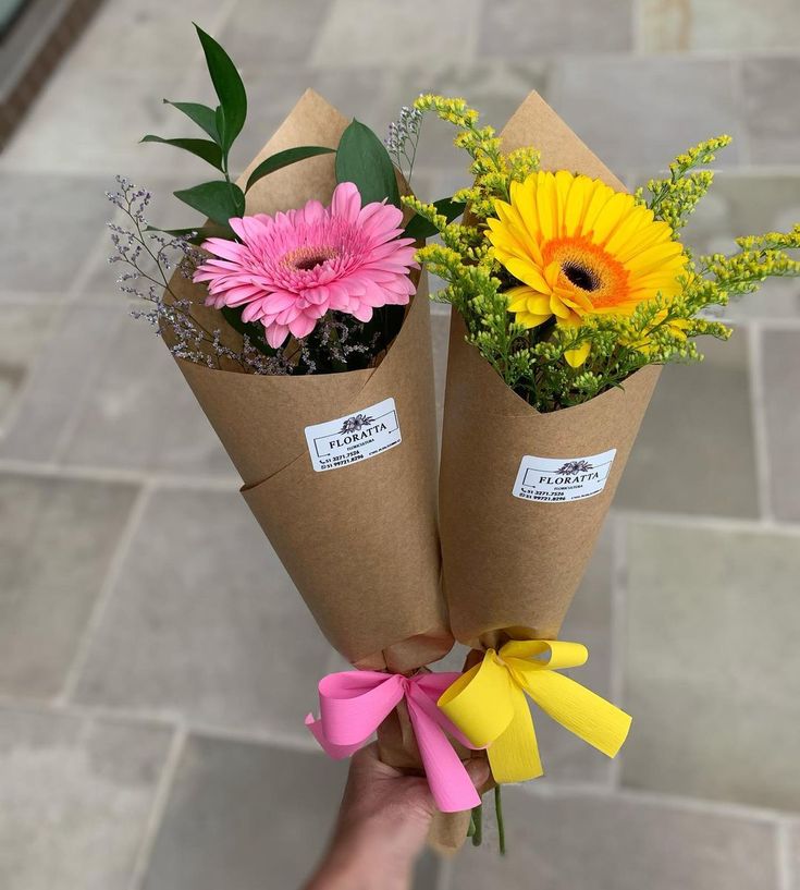 two flowers are wrapped in brown paper and tied with pink, yellow and green ribbons