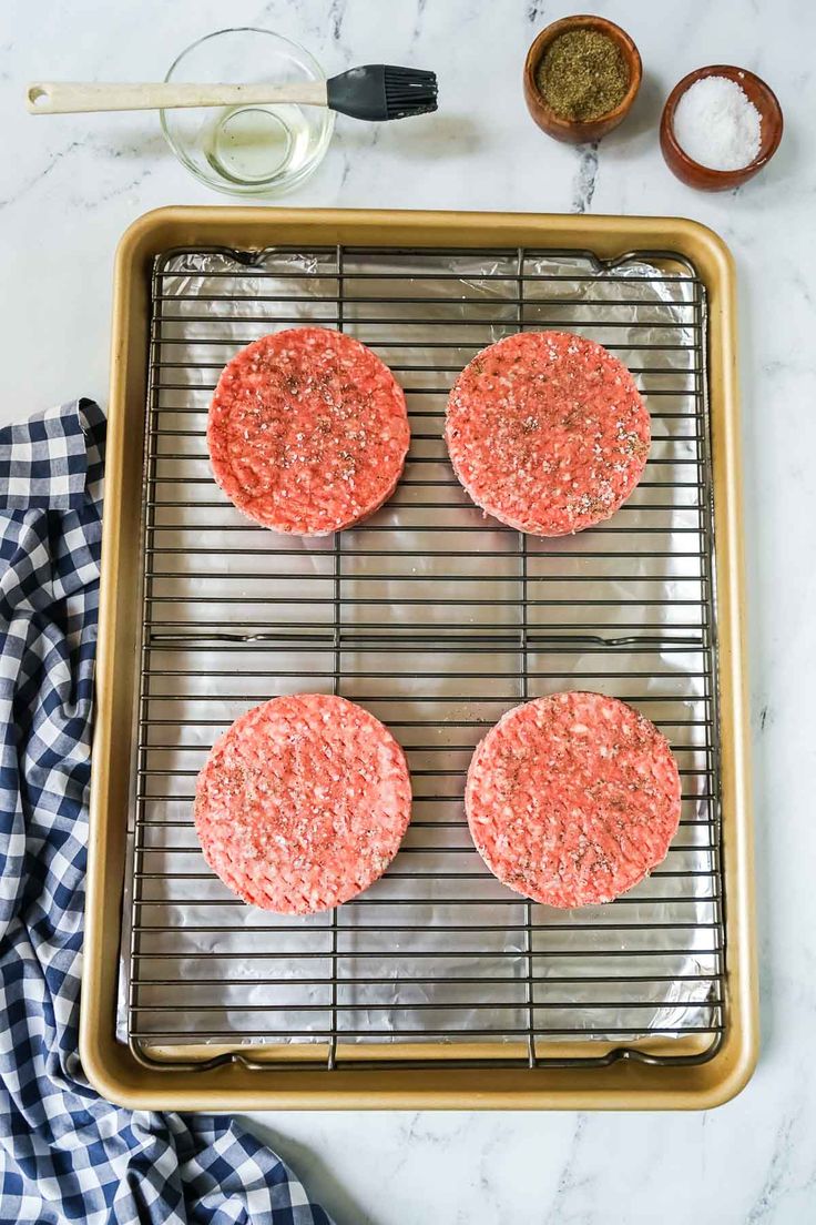 three hamburger patties on a cooling rack with seasoning and salt in the background