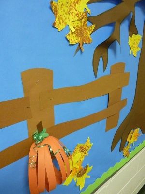 a bulletin board with fall leaves and paper pumpkins on it's side, in front of a blue wall