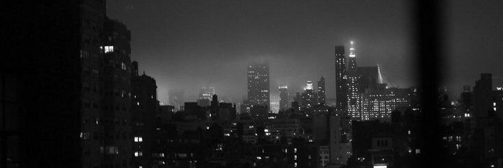 black and white cityscape at night with skyscrapers lit up in the distance