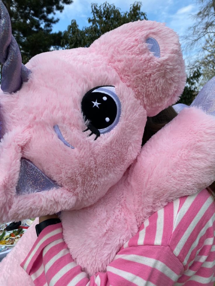 a pink stuffed animal with big eyes is being held by a woman in striped shirt