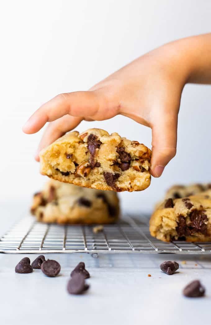 a person picking up a chocolate chip cookie from a cooling rack