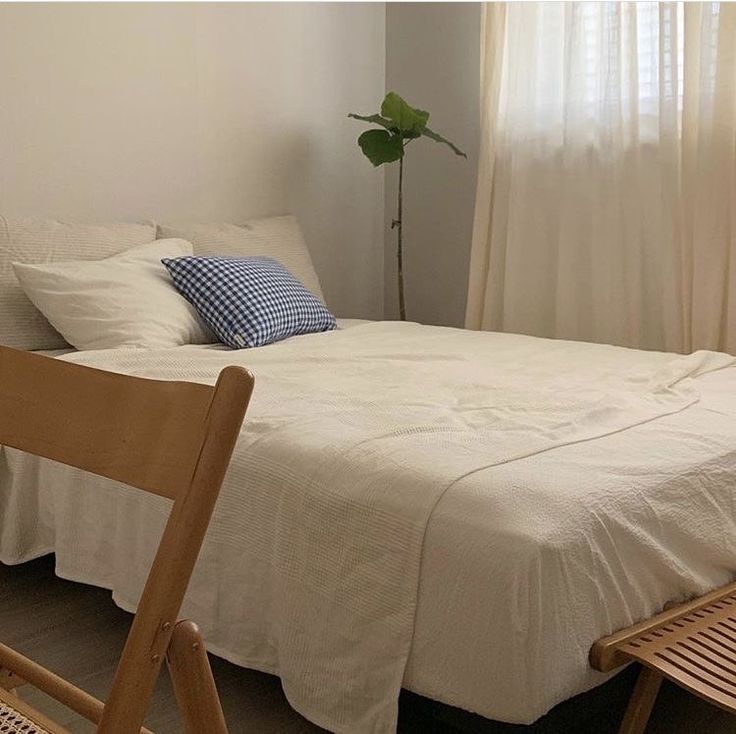 a white bed sitting in a bedroom next to a wooden chair and potted plant