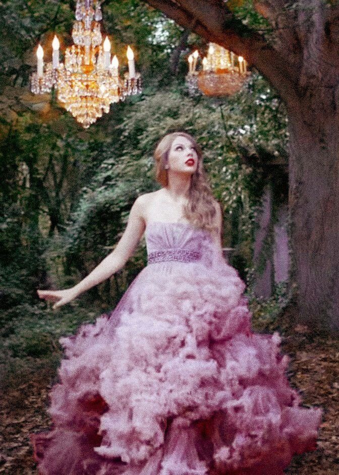 a woman in a pink dress standing under a tree with chandelier hanging from it's branches