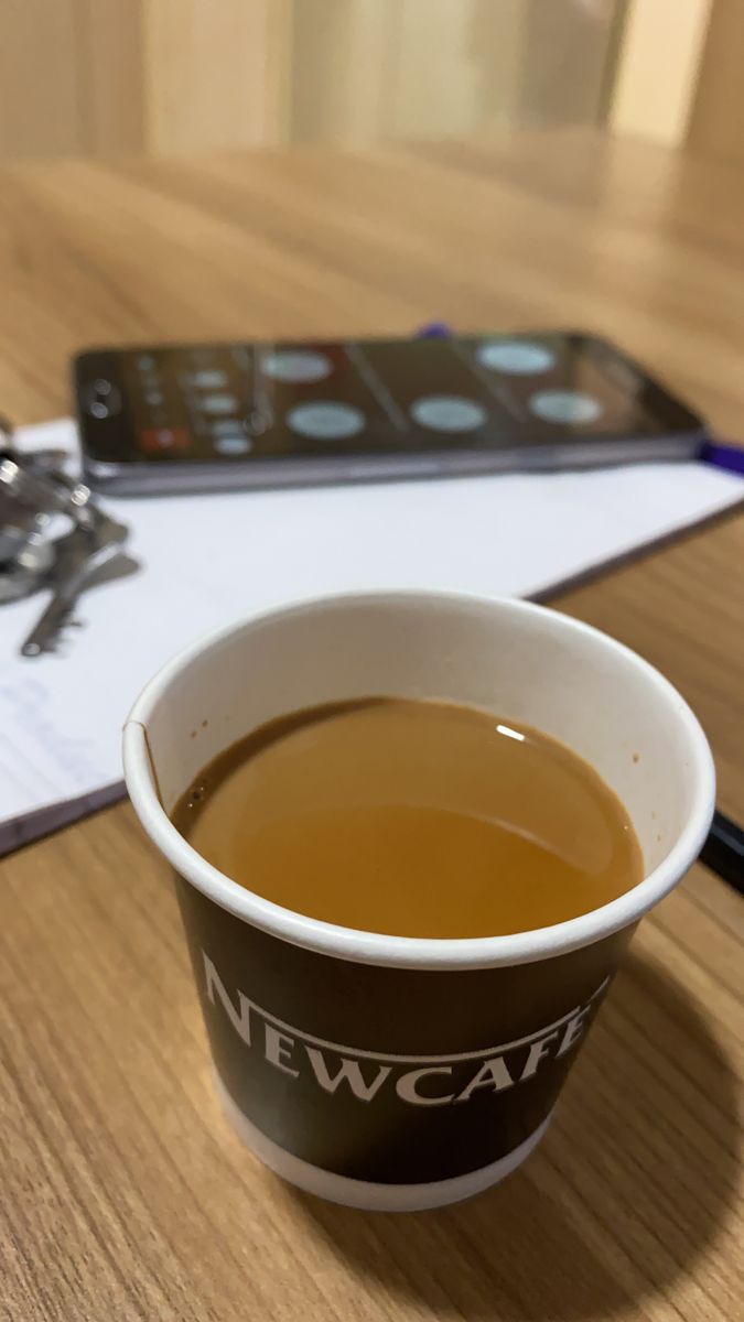 a cup of coffee sitting on top of a wooden table next to a cell phone