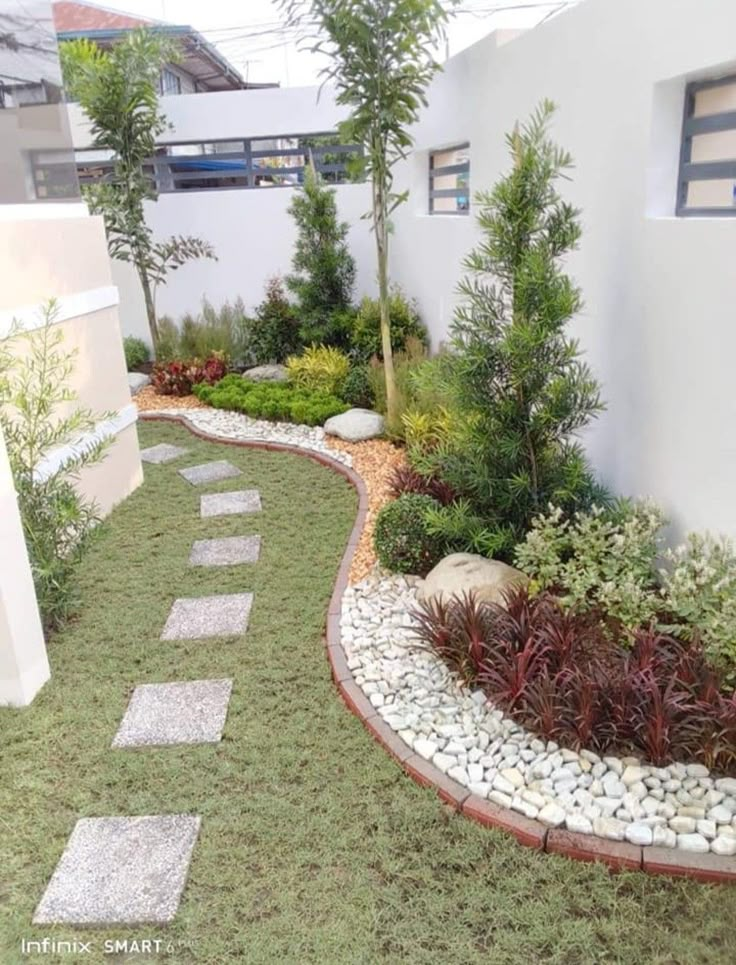 a small garden with rocks and plants in the center, along side a white building