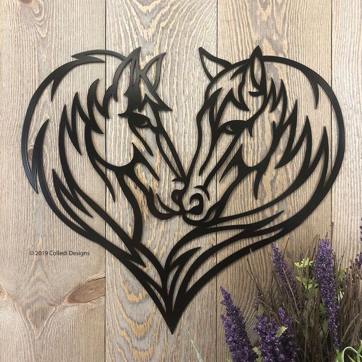 a metal heart with two wolf heads cut out of it on a wooden wall next to purple flowers