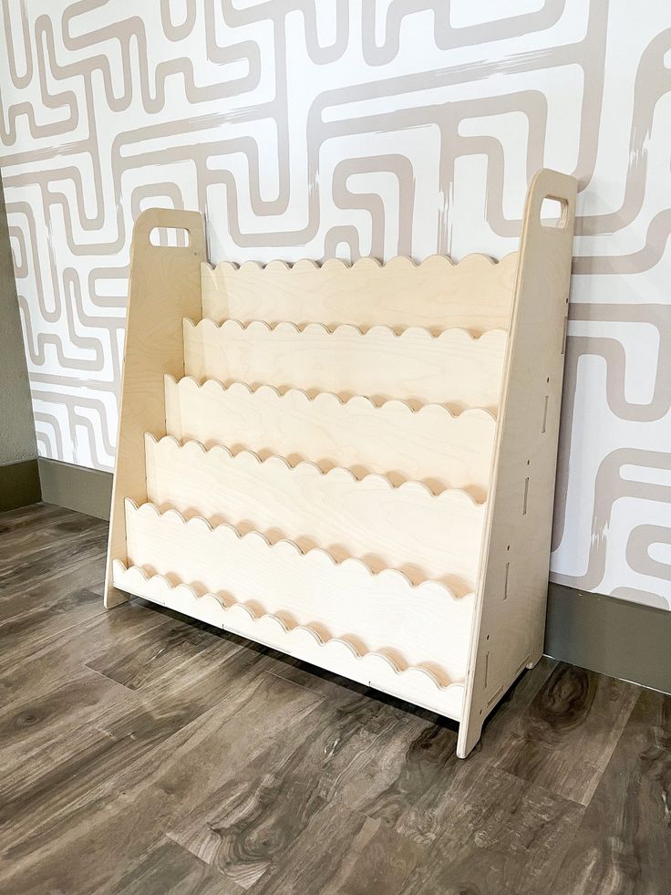 a wooden toy crib sitting on the floor in front of a wallpapered background