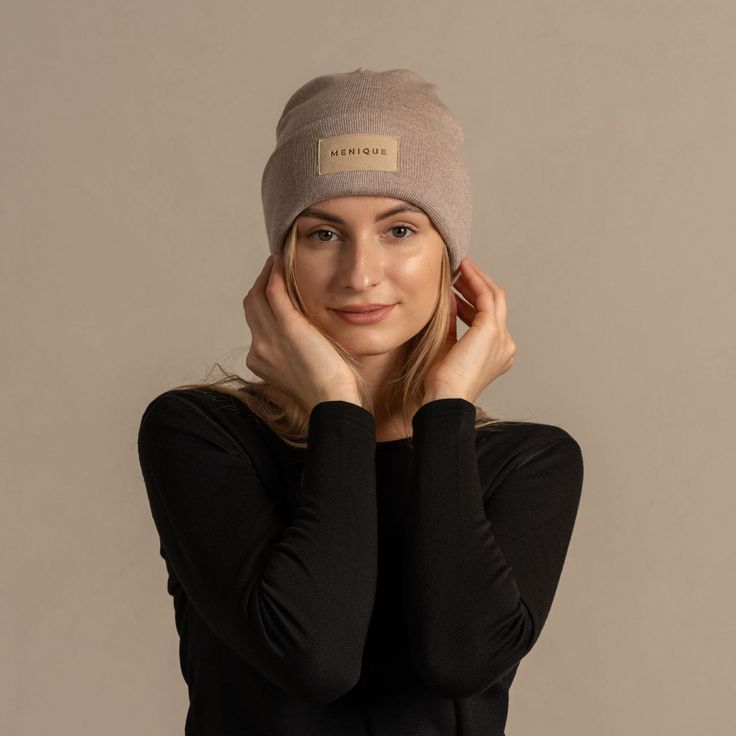 Woman wearing merino wool long sleeve top and knitted merino wool beanie with MENIQUE logo Cream Knitted Beanie For Winter, Knitted Cream Beanie For Winter, Beige Hats For Cold Weather, Beige Beanie Bonnet For Fall, Beige Beanie For Fall Cold Weather, Cream Winter Hats For Everyday, Beige Beanie For Cold Weather In Winter, Cozy Beige Hat For Outdoor, Cozy Beige Bonnet For Fall