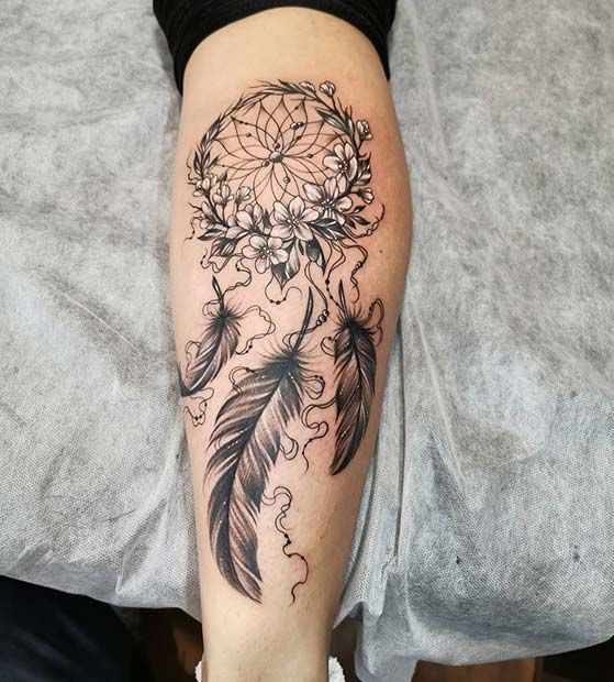 a woman's leg with a black and white dream catcher tattoo on her arm