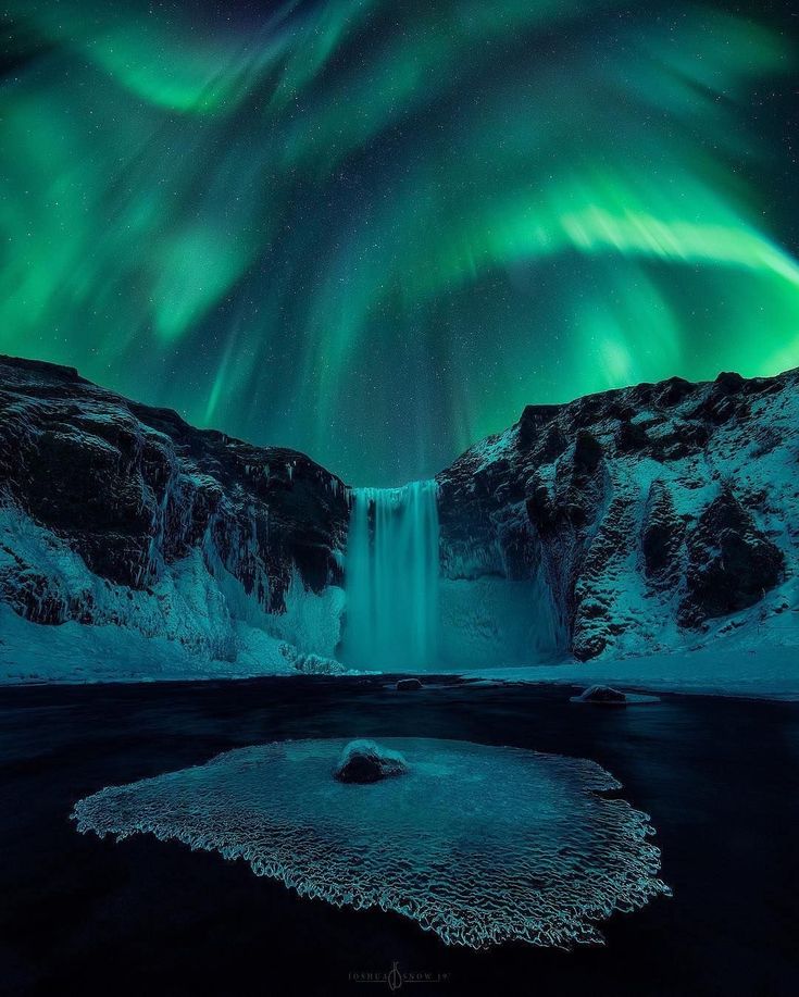 the aurora bore is lit up in the night sky above a waterfall and snow covered mountains