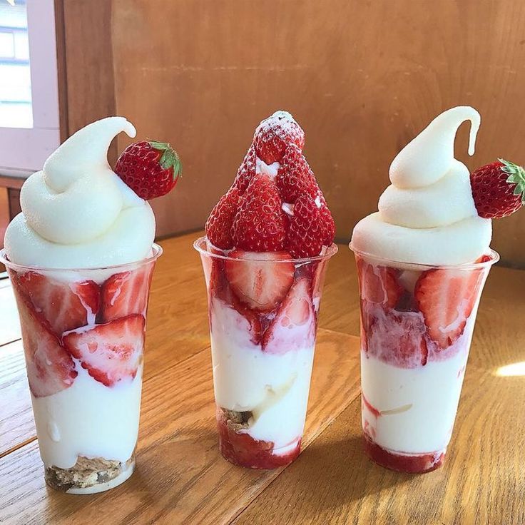 three cups with strawberries and whipped cream in them on top of a wooden table