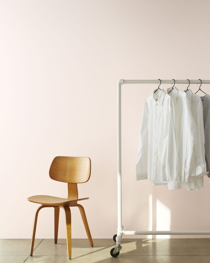 a white shirt hanging on a rail next to a chair and a rack with clothes