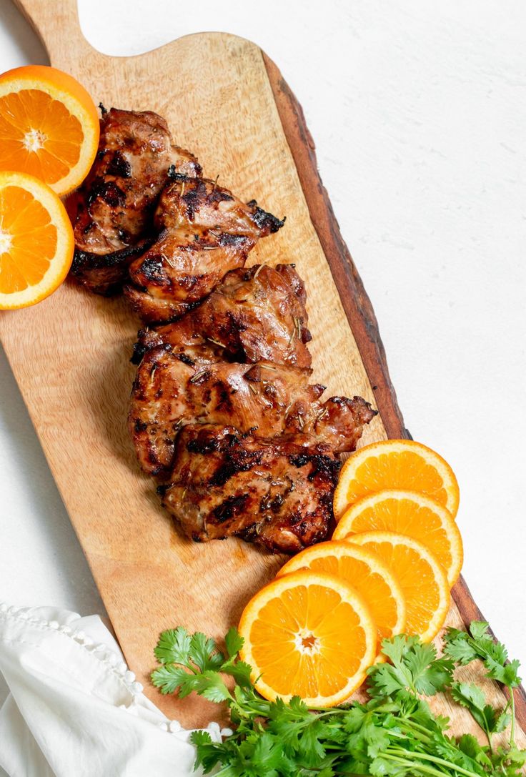 some meat and oranges on a cutting board with garnishes next to it