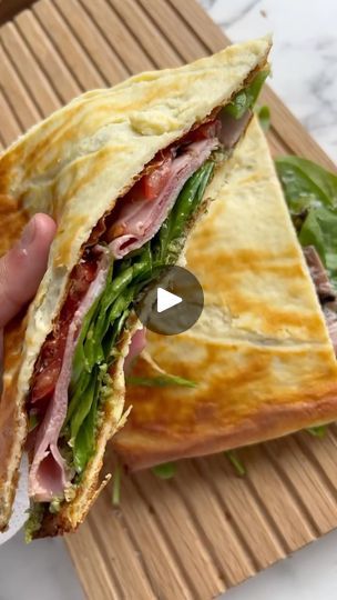 a person holding a sandwich with meat and vegetables in it on top of a cutting board