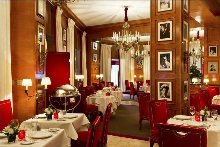 a dining room with red chairs and white tablecloths, chandeliers and pictures on the wall