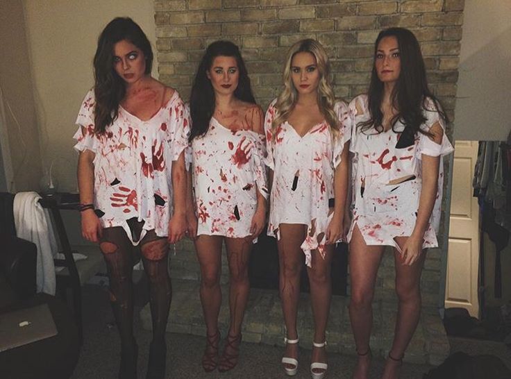 four women dressed in white dresses with blood all over their bodies and legs, standing next to a brick wall