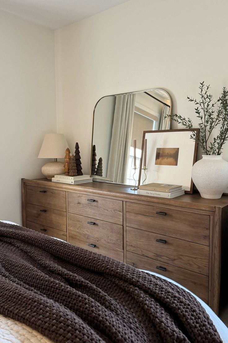 a bedroom with a bed, dresser and mirror on it's sideboard in front of a window