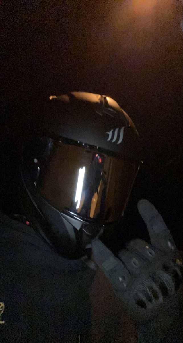 a motorcycle helmet sitting on top of a person's hand in the dark with light coming from behind it