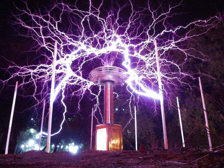 lightning strikes in the night sky over a tower with several lights on it and some trees