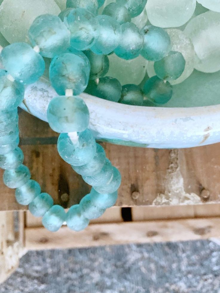 a close up of some glass beads on a wooden table with a bowl in the background