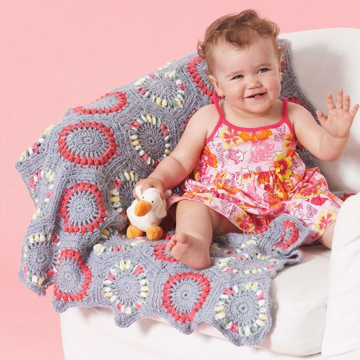 a baby sitting on a chair with a blanket over her and holding a stuffed animal