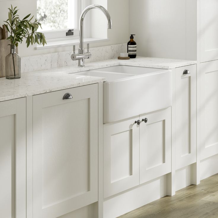 a kitchen with white cabinets and marble counter tops is pictured in this image, there are plants on the window sill