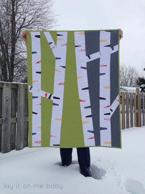 a person holding up a quilt made to look like birch trees in the winter snow