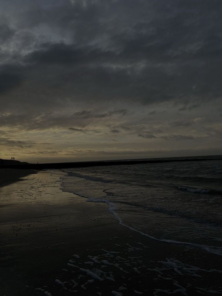 the sun is setting at the beach with dark clouds