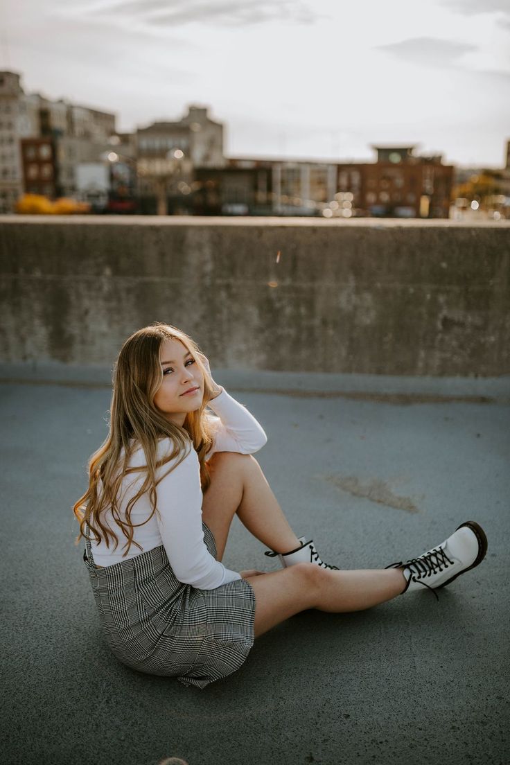 a young woman sitting on the ground with her legs crossed and looking at the camera