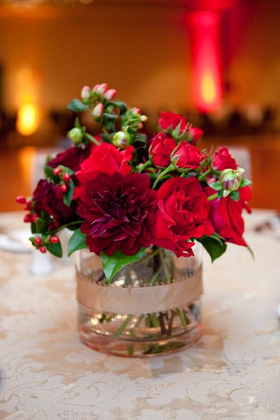 a vase filled with red flowers sitting on top of a white tablecloth covered table