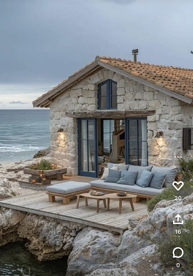 a stone house sitting on top of a rocky cliff next to the ocean with an outdoor seating area