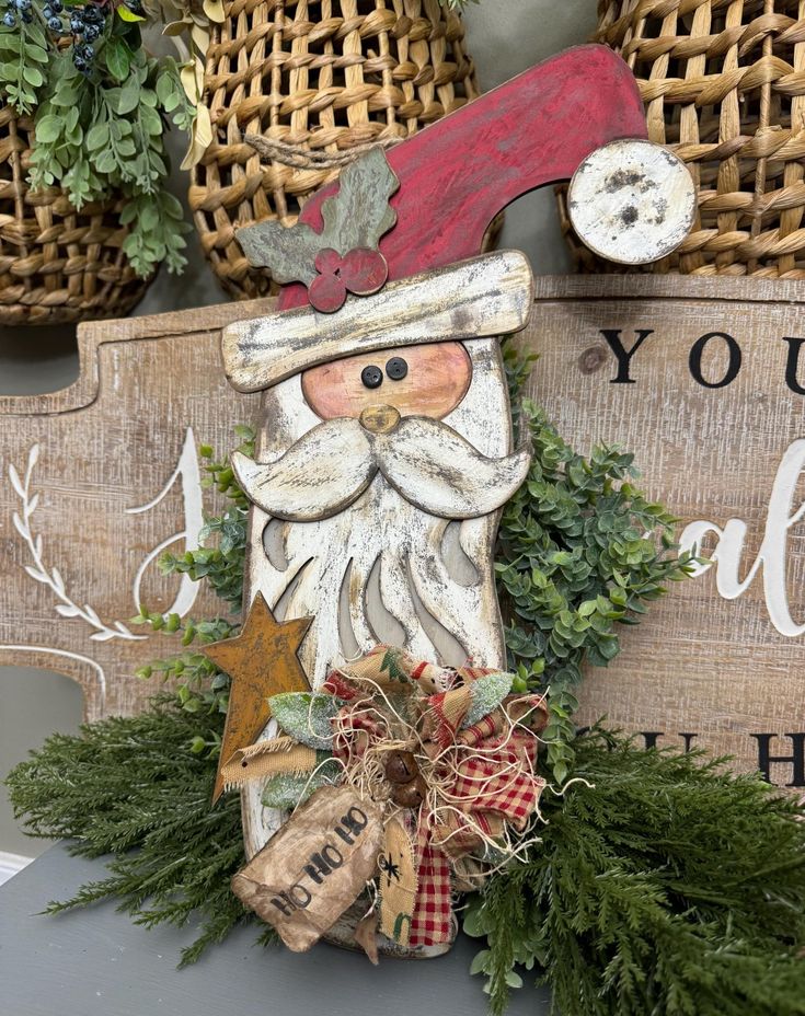 a wooden sign with a santa clause on it's face and some evergreens