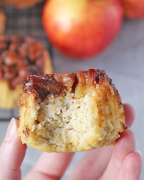 a hand holding a half eaten pastry in front of an apple and cinnamon muffin