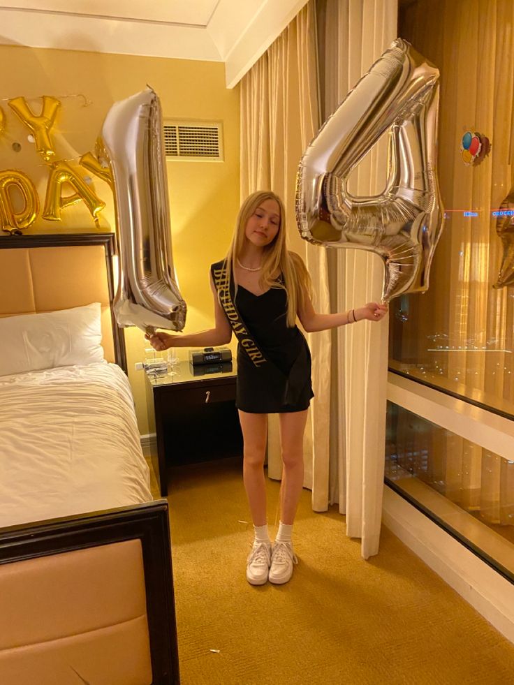 a woman in a black dress holding some silver balloons