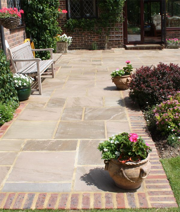 an outdoor patio with potted plants and flowers on the ground in front of a brick building