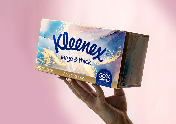 a person holding up a box of kleenex large and thick toilet paper in front of a pink background