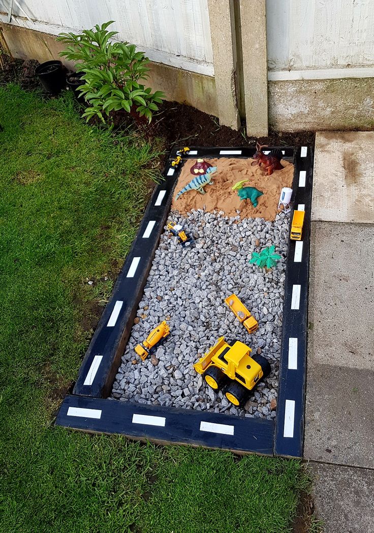 a toy construction truck is in the middle of a graveled area with grass and rocks