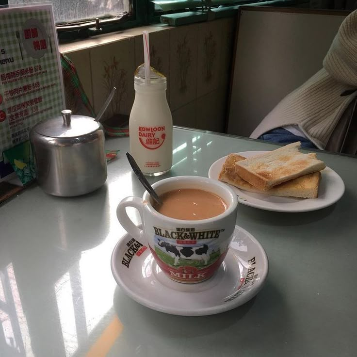 there is a cup of coffee on the table with toast and milk next to it