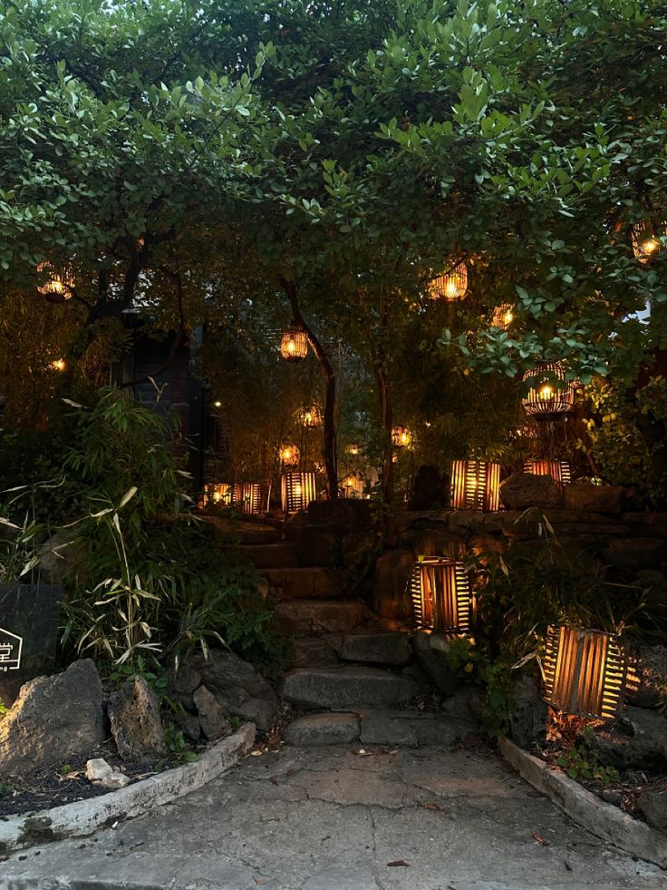 a stone path leading up to a building with lit lanterns on the trees above it