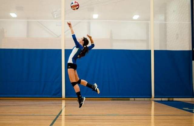 a female volleyball player jumping up to hit the ball with her racket in an indoor court