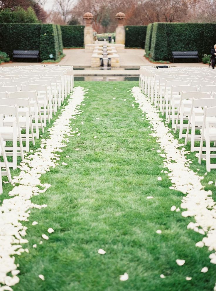 the aisle is lined with white flowers and petals, along with greenery on either side