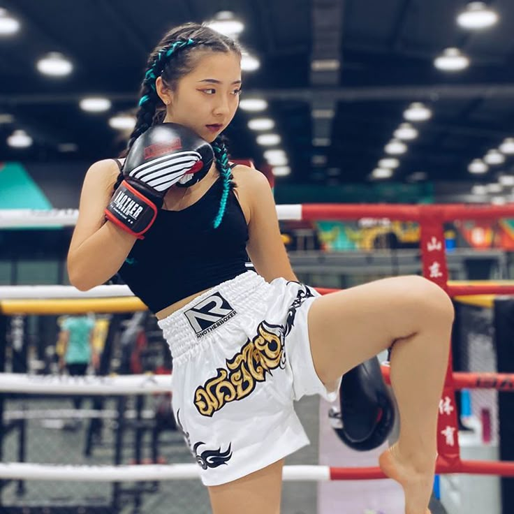 a young woman wearing boxing gloves standing on one leg in the middle of a kickbox ring