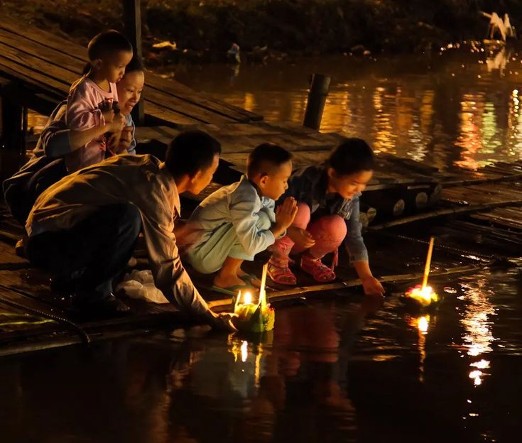 several children are sitting on the dock with candles in front of them as they look at something